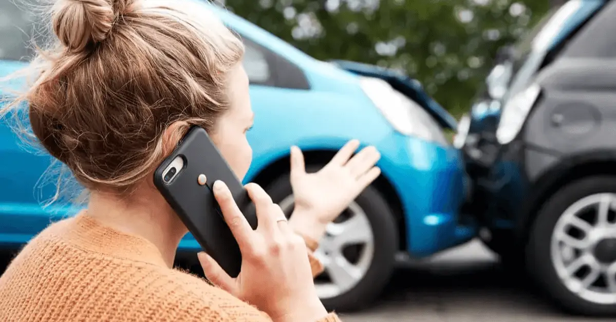 A woman on her phone gesturing towards two cars involved in a rear-end collision, with visible damage to both vehicles