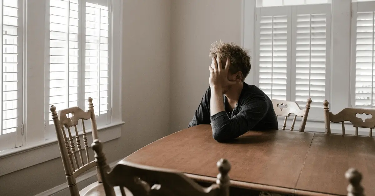 Person sitting at a wooden table with their head resting on their hand, appearing distressed after a DWAI