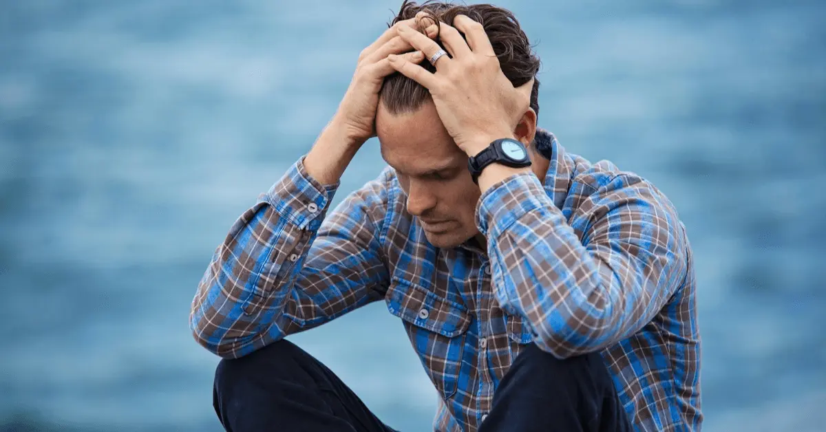 An overwhelmed man sitting by water with hands on his head, representing the emotional toll of a DUI charge