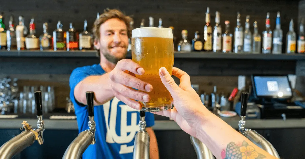 Smiling bartender handing a pint of beer to a customer in a bar