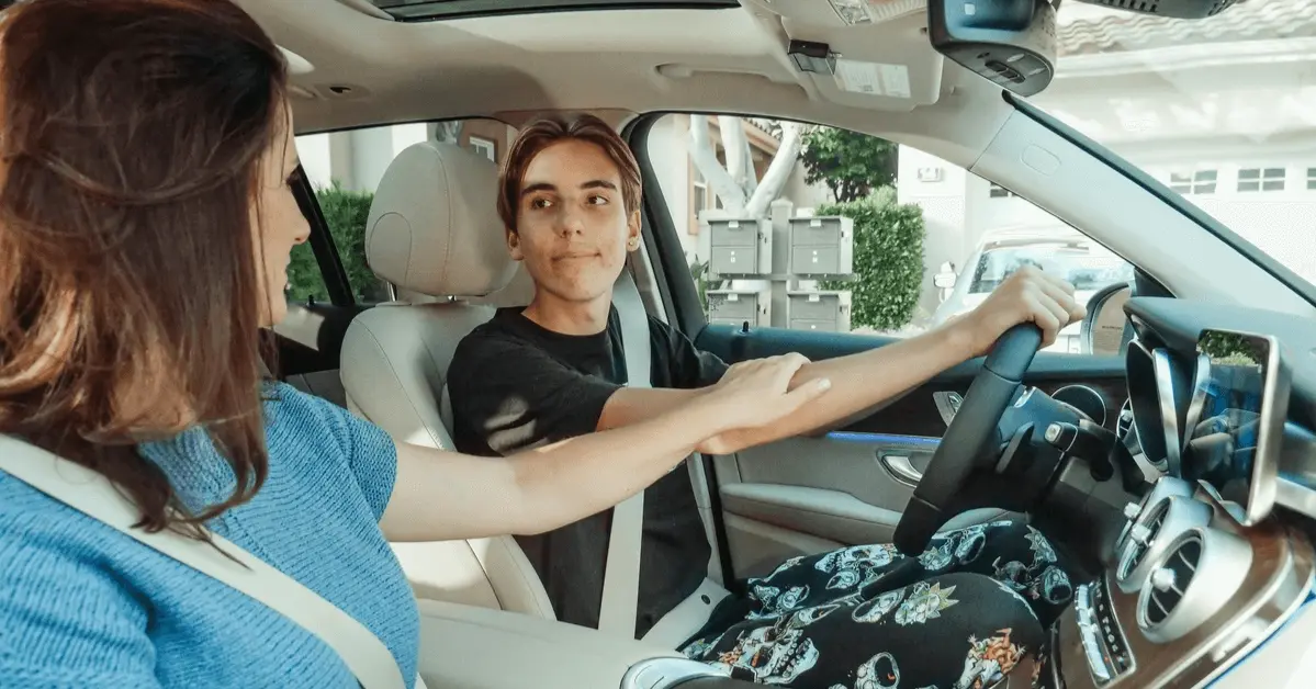 Parent guiding a teenage driver in a car, holding their arm to offer advice or encouragement