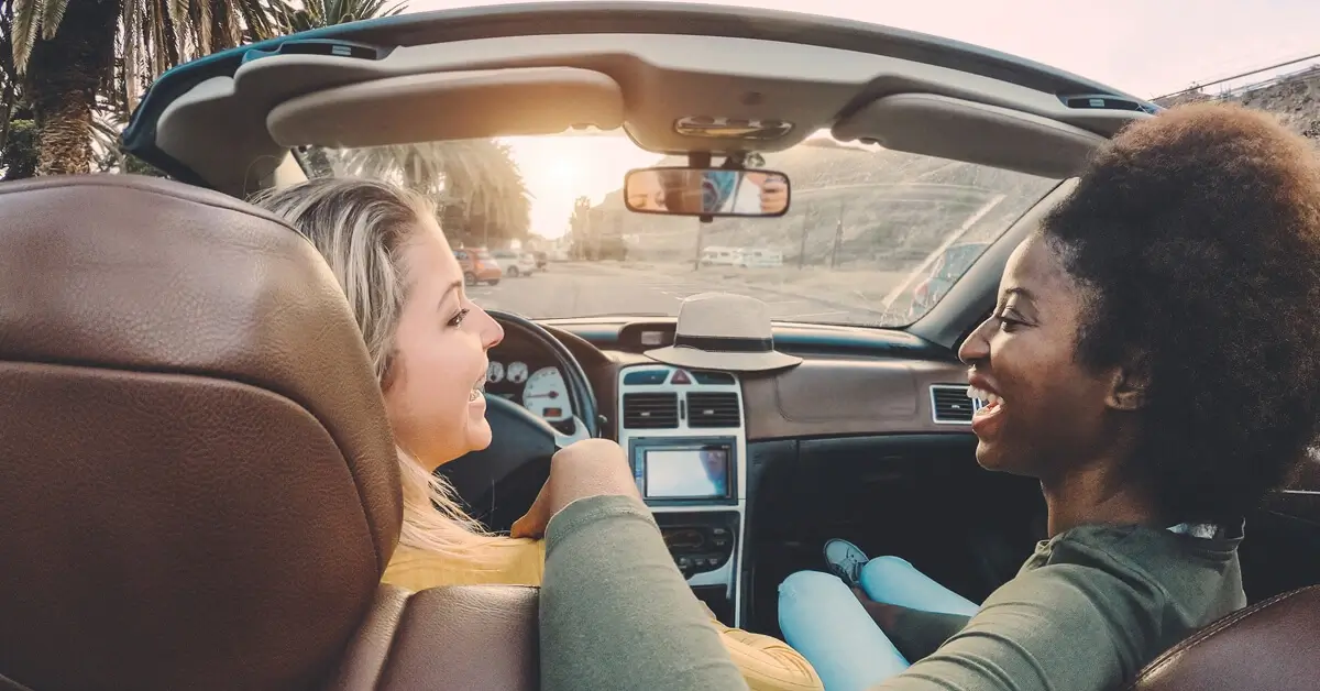 Two women smiling and enjoying a drive in a convertible car on a sunny day