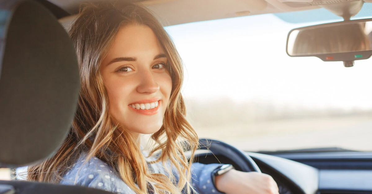 Smiling young woman seated in the driver’s seat of a car, looking back over her shoulder