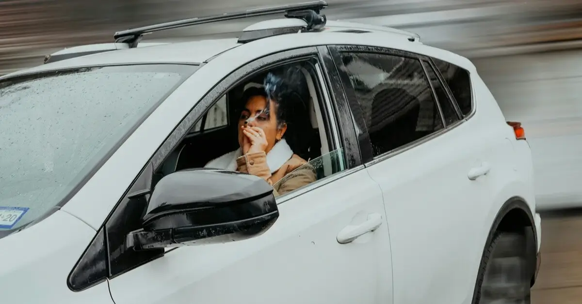 Driver in a white SUV smoking with the window down on a rainy day