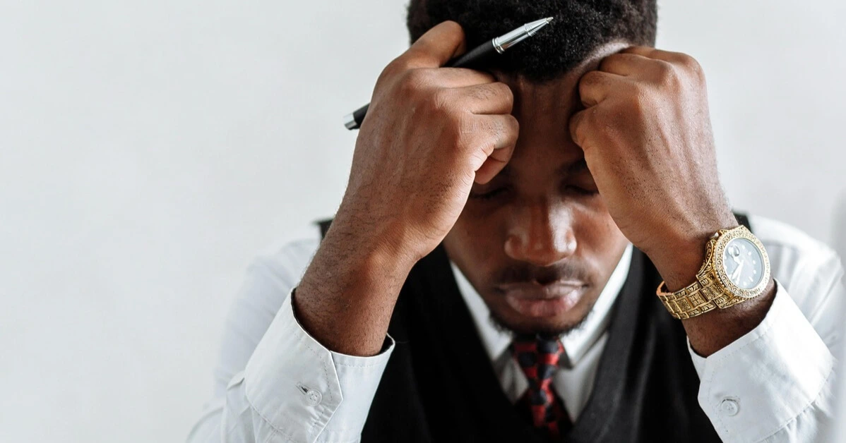 Professional man sitting with his head in his hands, appearing stressed while holding a pen