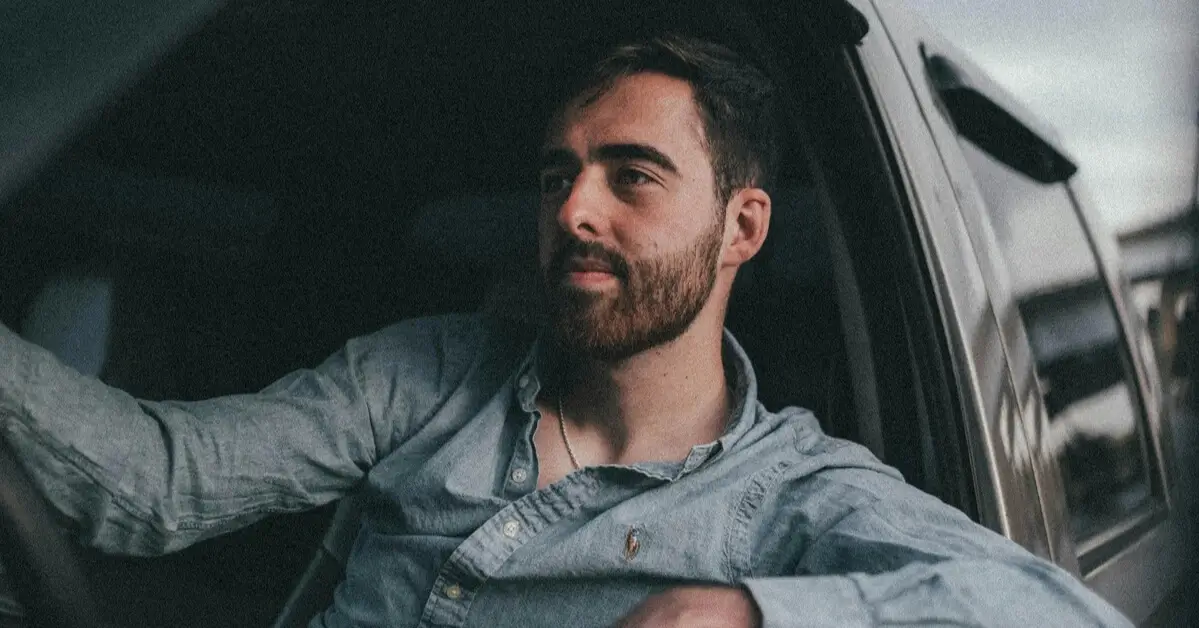 Man sitting in the driver’s seat of a car, gazing thoughtfully out the window