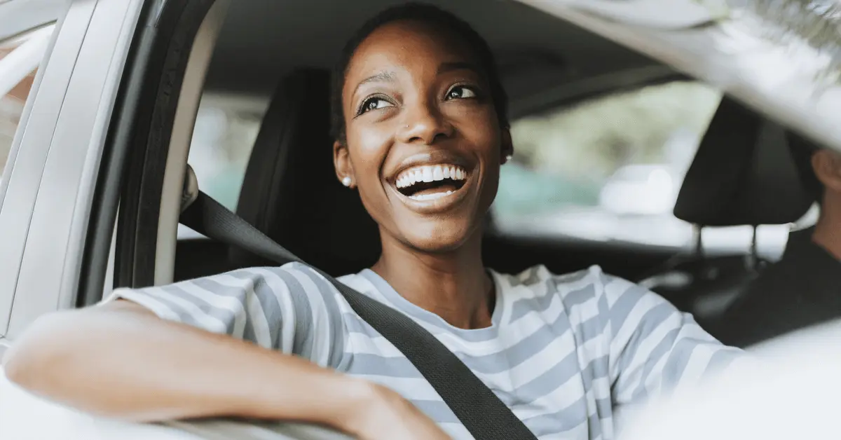 Smiling woman sitting in a car with her arm resting on the window, looking outside