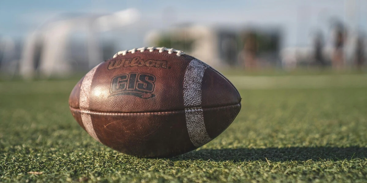 A football resting on a green field under a clear sky