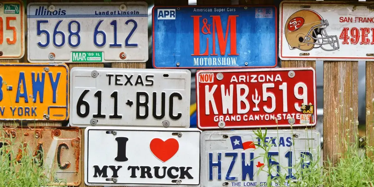 Collection of license plates, including ones from Texas, Arizona, and Illinois, displayed on a wooden fence