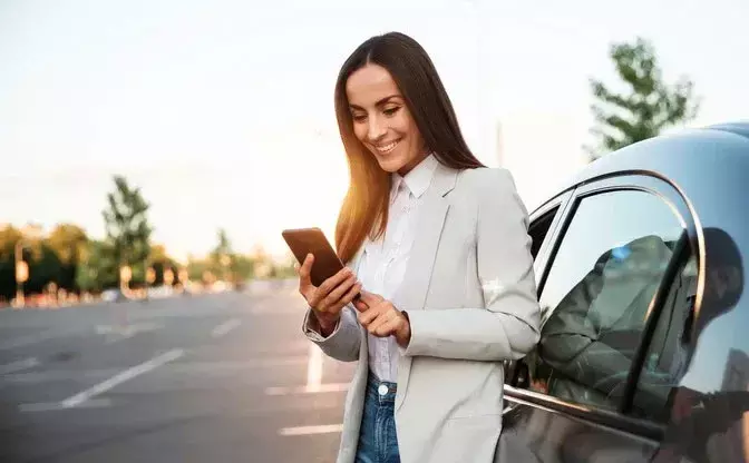 Woman standing next to a car, smiling while using the Keepr app on her phone
